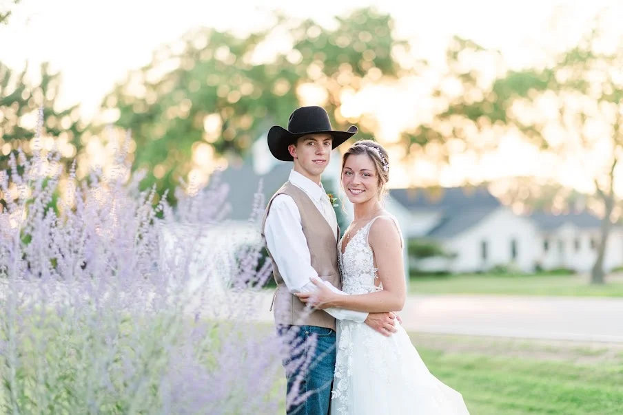 Bride and groom standing together at sunset near flowers in front of the farm