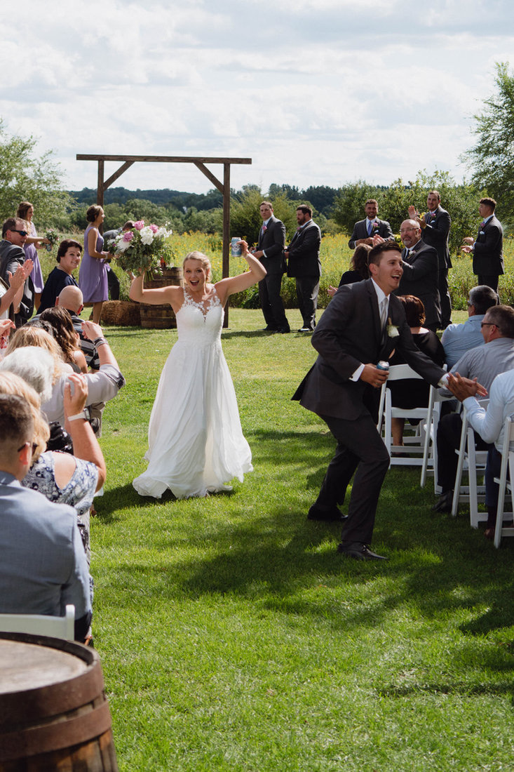 Bride and groom dancing down the aisle celebrating their marriage at Huser Farm outdoor wedding venue