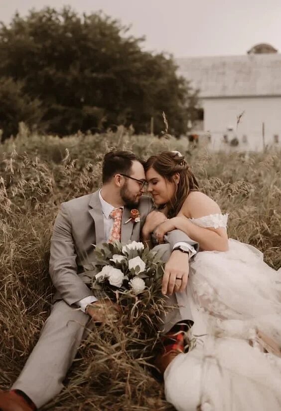 Bride and groom face to face laying in a golden field with the barn behind at a Wisconsin country wedding