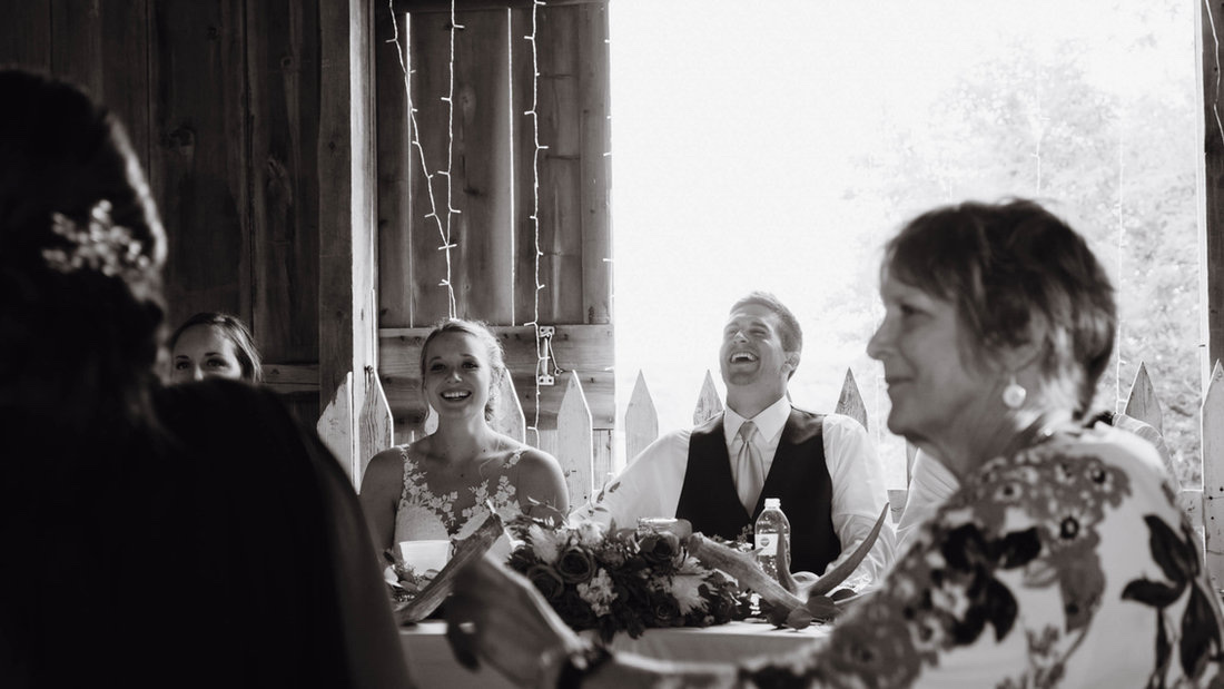 Bride and groom laughing around a table with family in the rustic wedding barn at Huser Farm
