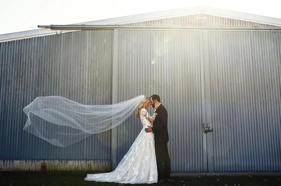Bride's veil blowing in the wind as she embraces the groom at a rustic Wisconsin wedding barn