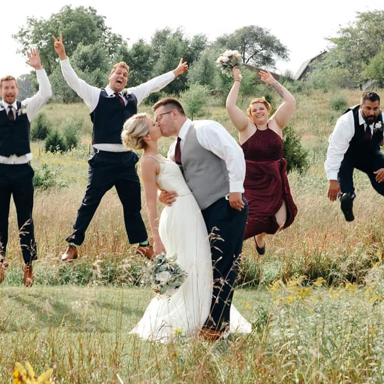 Joyful wedding party jumping in front of the barn at Huser Farm in Wisconsin